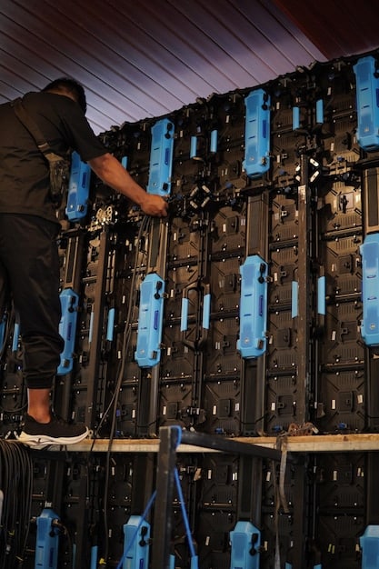 Close-up of a technician inspecting a row of advanced battery storage units in a clean, modern facility. Wires and connectors are visible, highlighting the complexity of the technology.